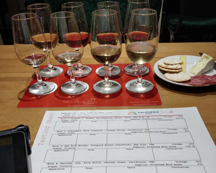 Tasting sheet with a list of wines and places for notes in the front, filled tasting glasses with white, rosé and red wine as well as a small plate with cheese and charcuterie.