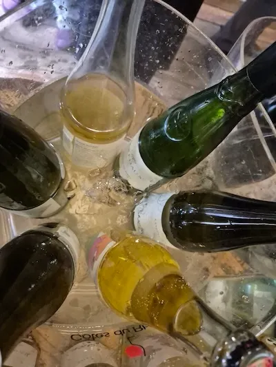 6 open white wine bottles in a wine cooler filled with ice.